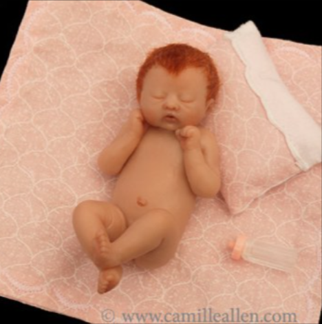 Asta, a miniature sculpted newborn with red hair asleep on a pink quilt beside a tiny pillow and bottle